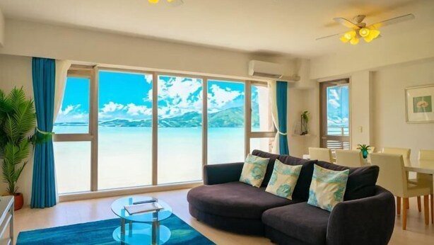 A living room with a sofa, a coffee table, and a view of the sea. - Lala Court Seaside Yagaji (Nago)