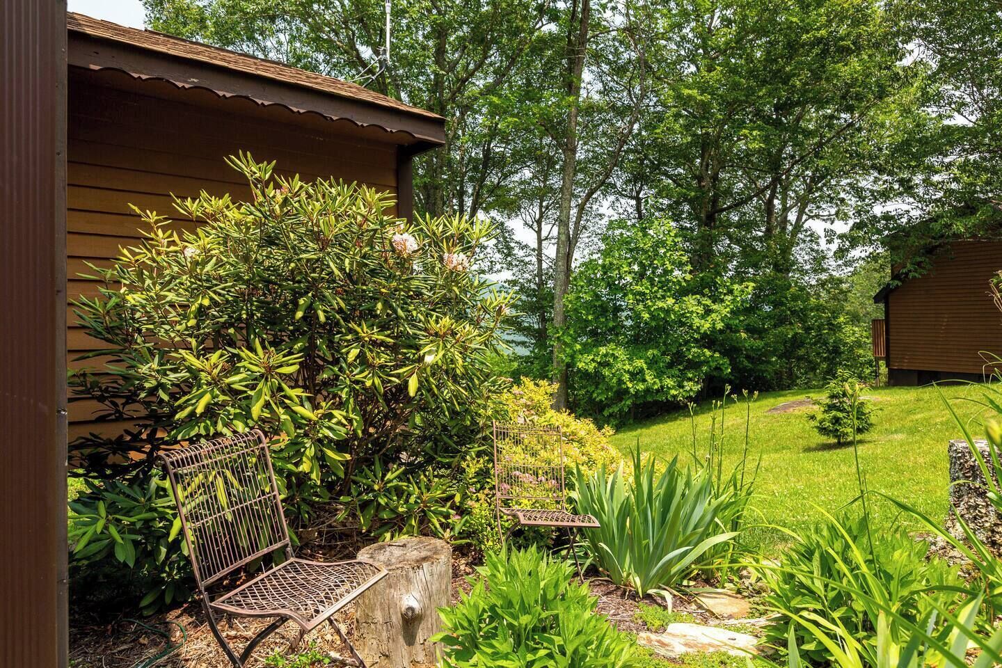 A wooden cabin with a metal bench and a garden with various plants and trees.