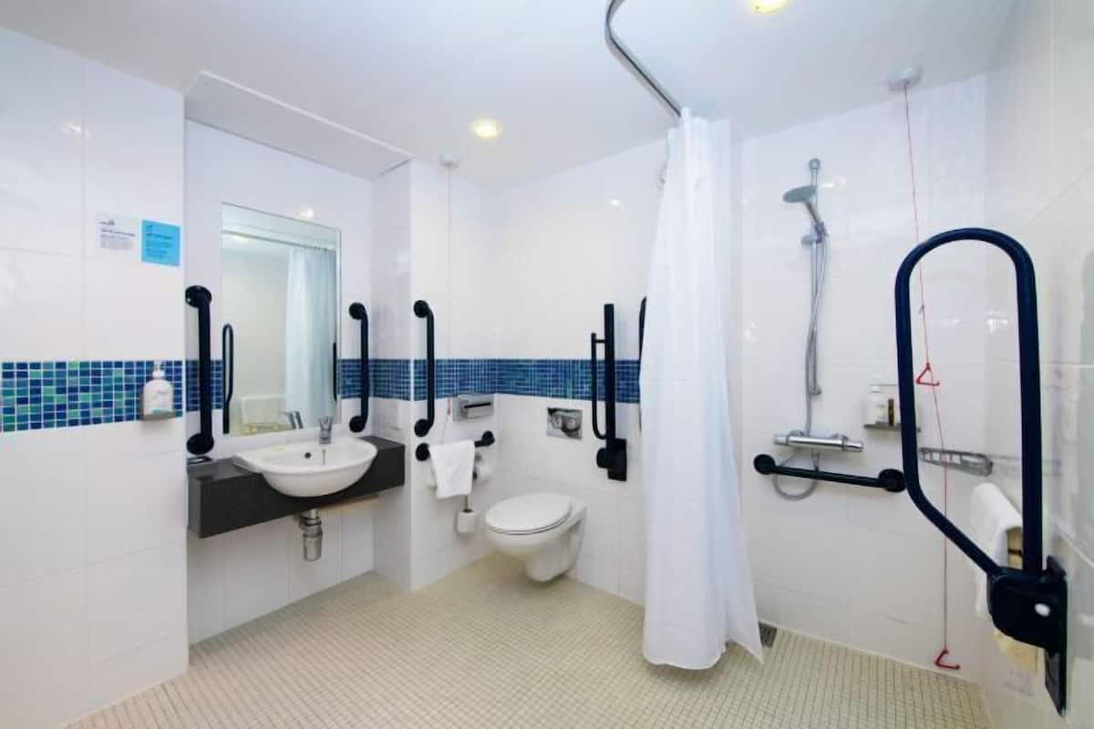 A bathroom with a sink, toilet, shower, and handrails.