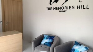 A room with a wooden door, a wall-mounted sign reading "The Memories Hill Phuket," two grey armchairs with blue cushions, and a small white table. - The Memories Hill Phuket (Phuket)