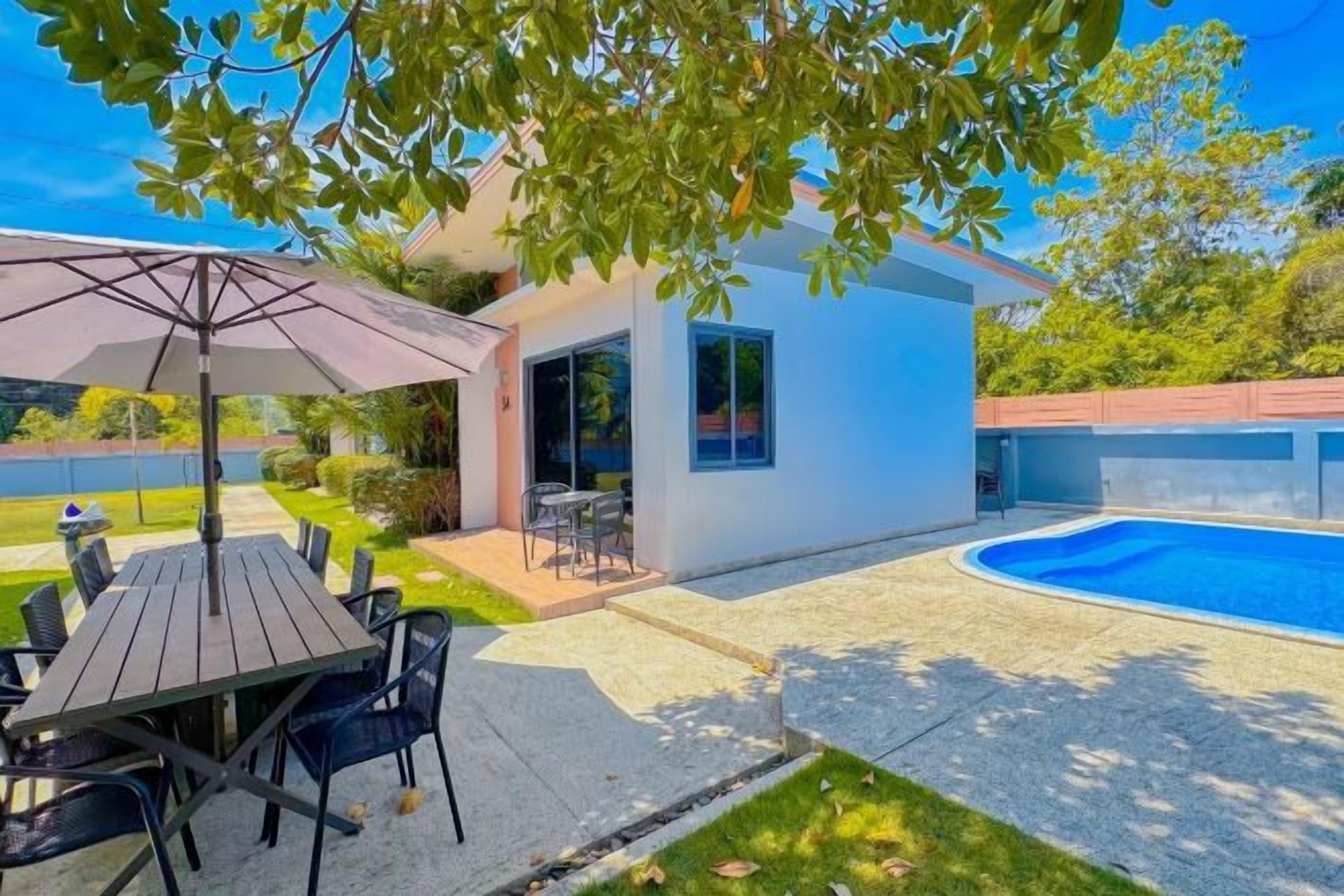 Une maison moderne dotée d’une piscine, de mobilier de jardin et d’un petit jardin.