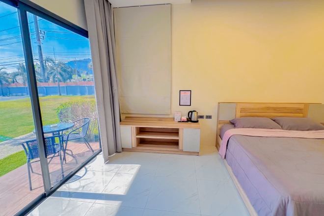 A hotel room with a bed, a desk, and a large window overlooking a grassy area.