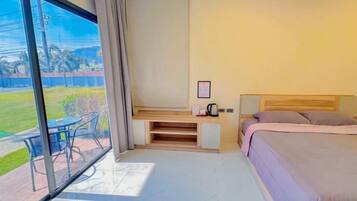 A hotel room with a bed, a desk, and a large window overlooking a grassy area.