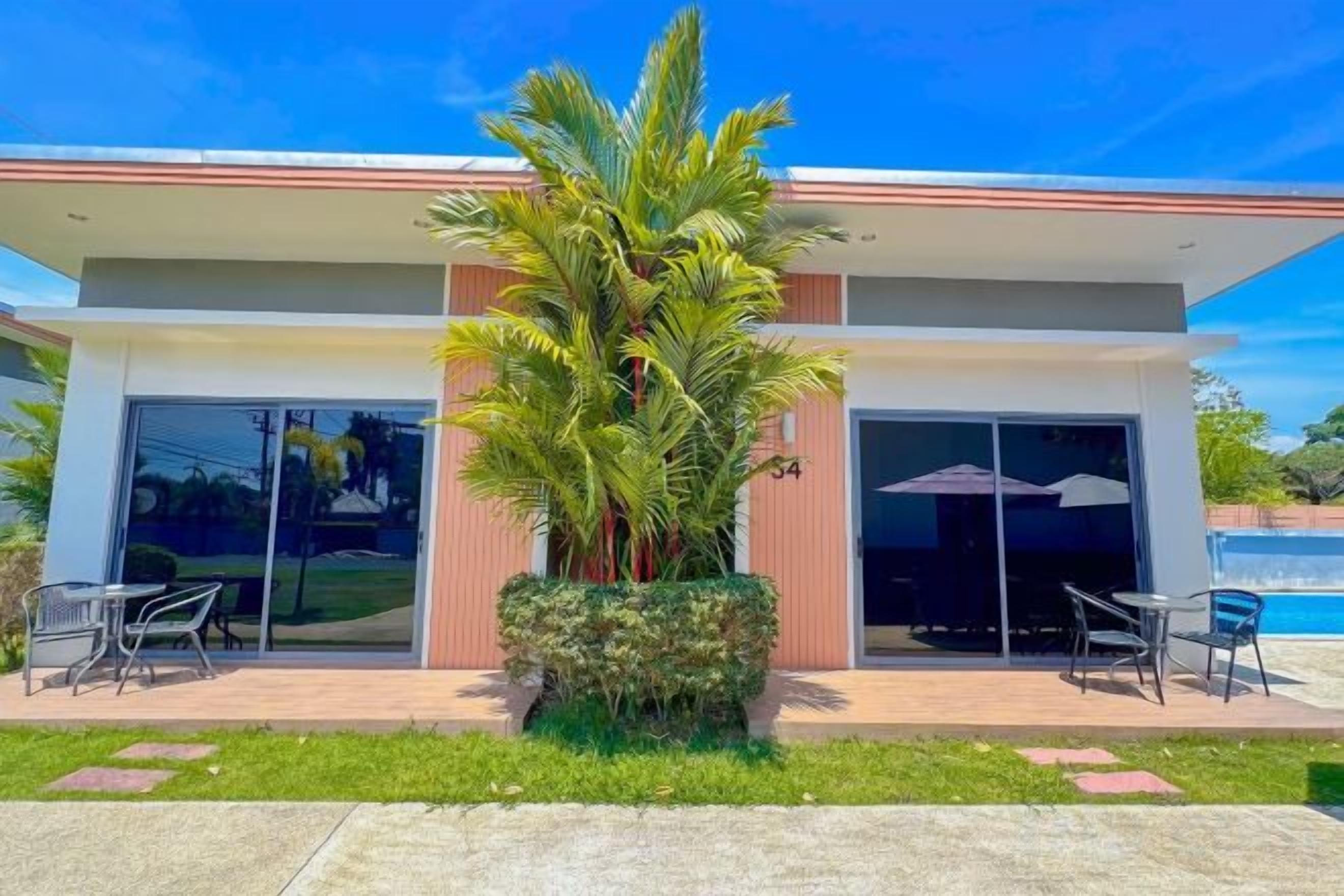 A modern building with a large glass door, a patio with outdoor furniture, and a palm tree.