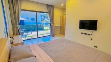 A hotel room with a bed, a TV, a sliding glass door to a balcony, and a small table with a kettle.