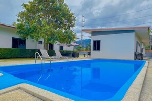 A swimming pool with a clear blue water surface, surrounded by a low wall and a paved area. There are lounge chairs and a small table under a tree. - The Memories Hill Phuket (Phuket)