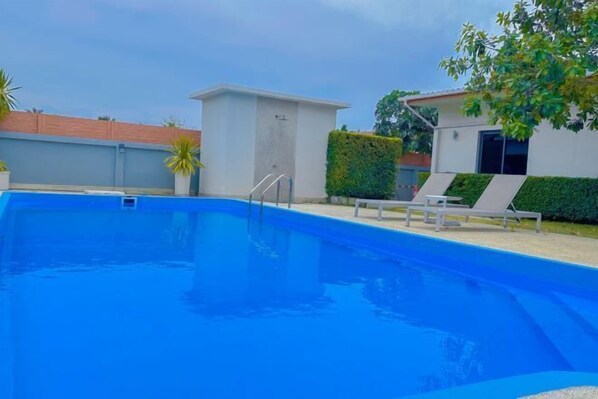 A swimming pool with a clear blue water, surrounded by a white building with a small window and a door. There are two lounge chairs and a potted plant near the pool. - The Memories Hill Phuket (Phuket)
