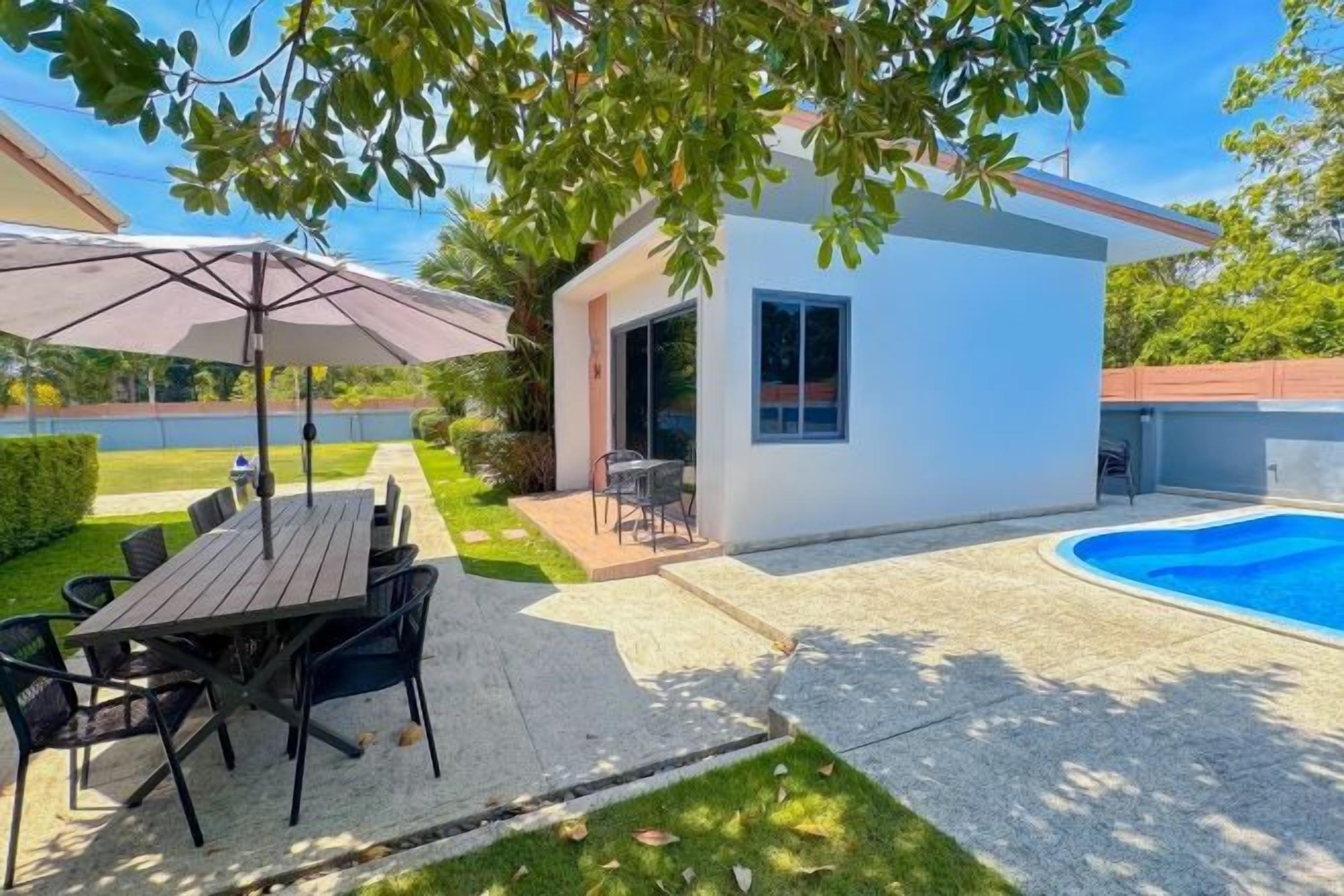 Un patio exterior moderno con una mesa de comedor y sillas, un pequeño edificio con una ventana y una piscina.