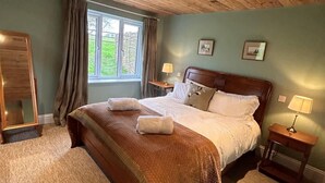 A bedroom with a wooden ceiling, a large bed with a headboard, two bedside tables with lamps, and a window with curtains. - Badgers Bolt - Idyllic rural apartment (Hungerford)