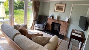 A living room with a sofa, a fireplace, a television, and a view of the outdoors. - Badgers Bolt - Idyllic rural apartment (Hungerford)