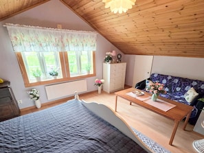 A bedroom with a bed, a dresser, a window with curtains, a sofa, and a table with a vase of flowers. - 6 Person Holiday Home in Lysekil (Lysekil)
