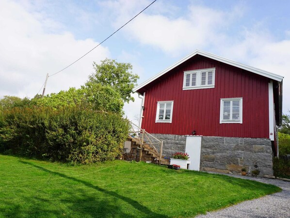 A red wooden house with white trim, a stone foundation, and a small porch with a wooden chair. - 6 Person Holiday Home in Lysekil (Lysekil)