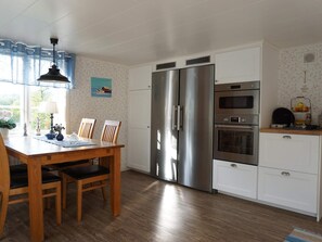 A modern kitchen with a double-door refrigerator, a built-in oven, and a microwave. There is a dining table with chairs and a window with curtains. - 6 Person Holiday Home in Lysekil (Lysekil)