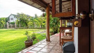 A covered outdoor area with a wooden ceiling, a tiled floor, and a view of a green lawn and house in the background.