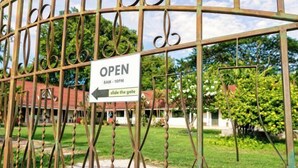 Uma entrada com portão e placa indicando horário de funcionamento das 8h às 22h, com instruções para abrir o portão.
