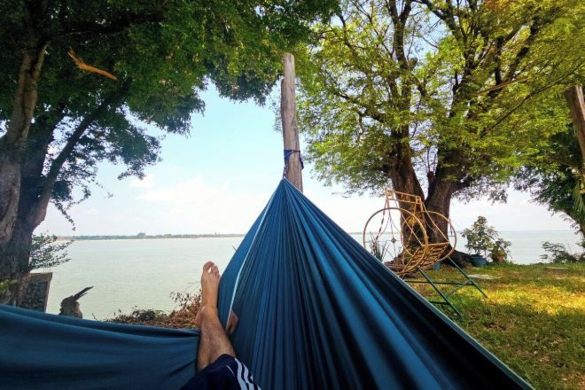 A hammock tied between trees with a view of a calm body of water.