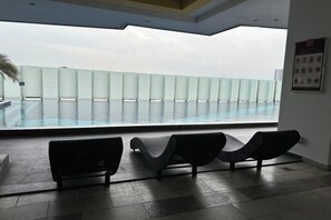 Uma área de piscina interior moderna, com espreguiçadeiras e uma barreira de vidro com vista para a piscina.