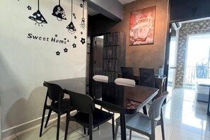 Un coin repas avec une table et des chaises noires, un mur orné d’une inscription « Sweet Home », et une vue sur l’extérieur.