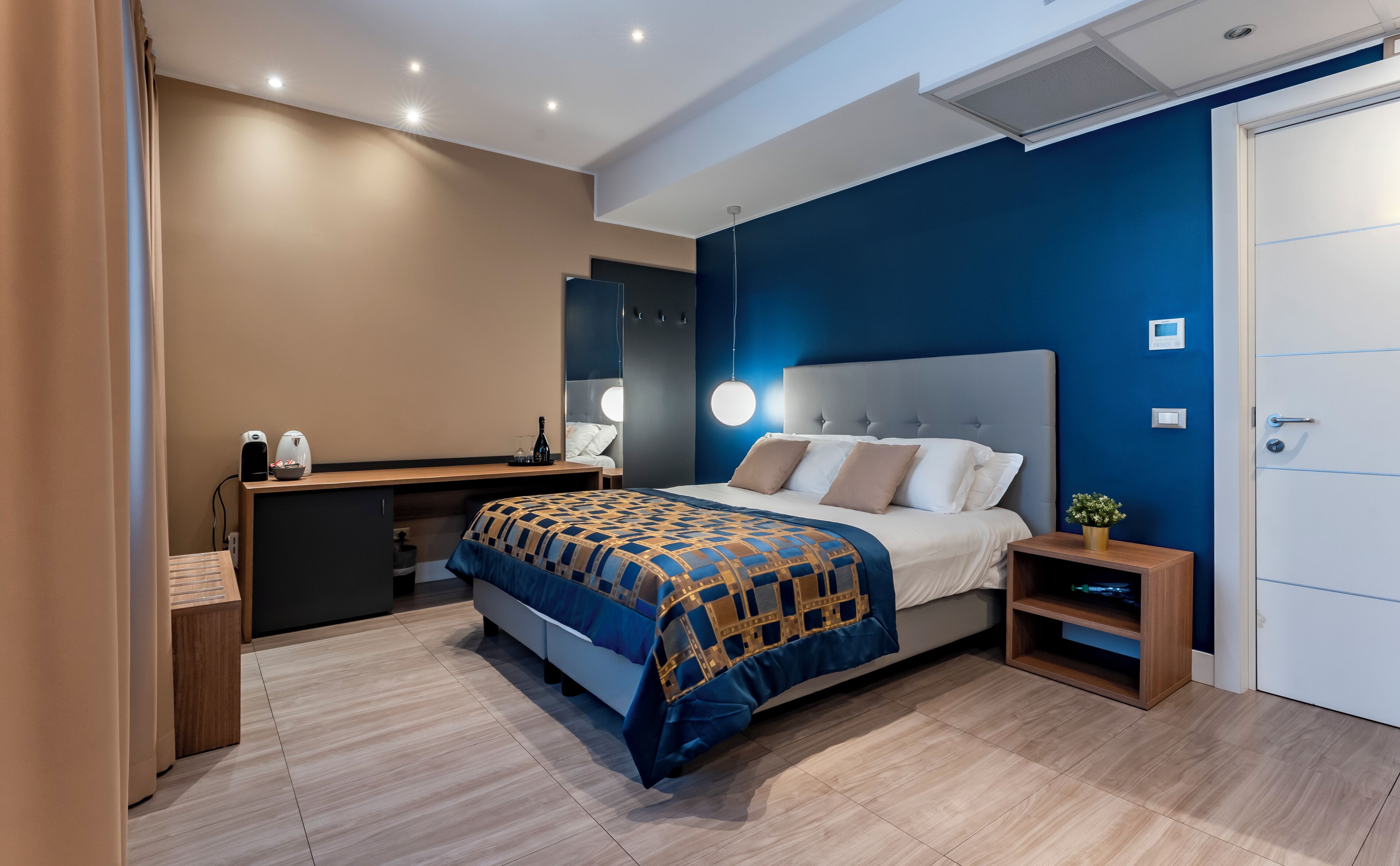 A modern bedroom with a large bed, bedside table, and a desk with a chair.