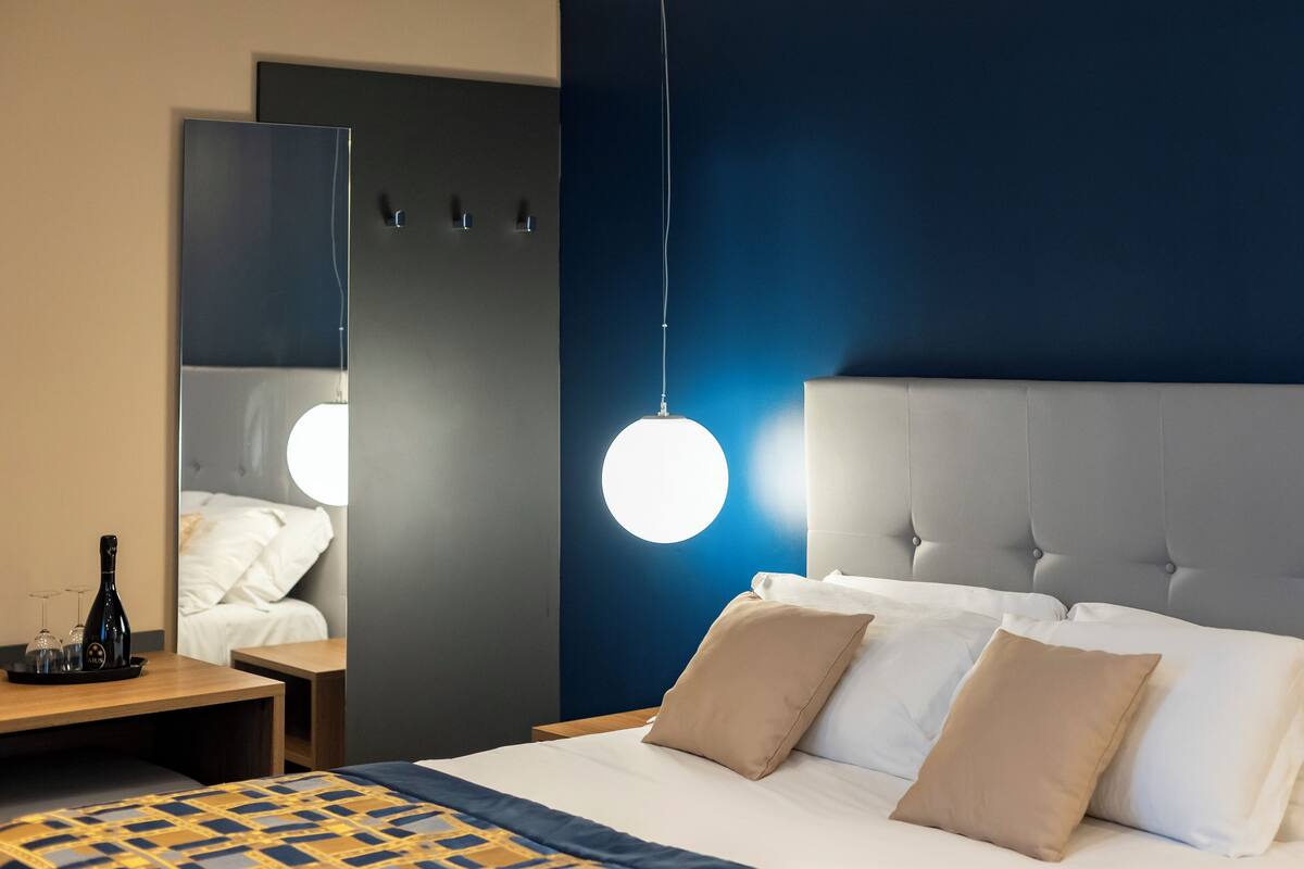 Habitación de hotel con una cama grande, una mesita de noche con una botella y vasos, y una lámpara colgante.