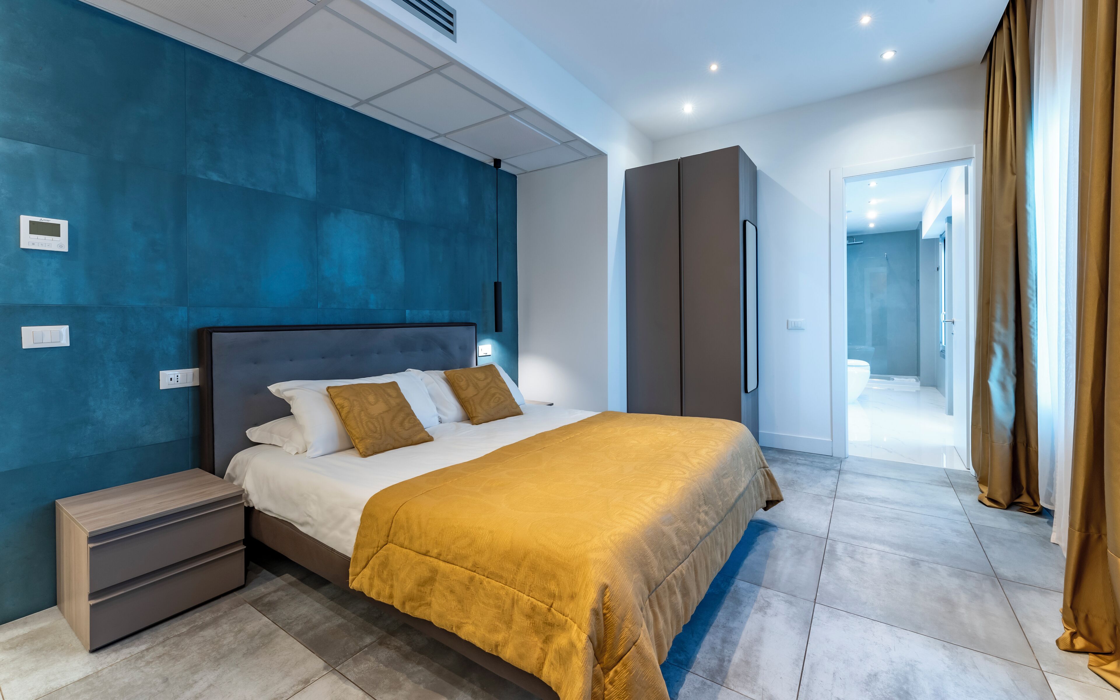 A modern hotel room with a large bed, a wardrobe, and a bathroom visible through an open door.