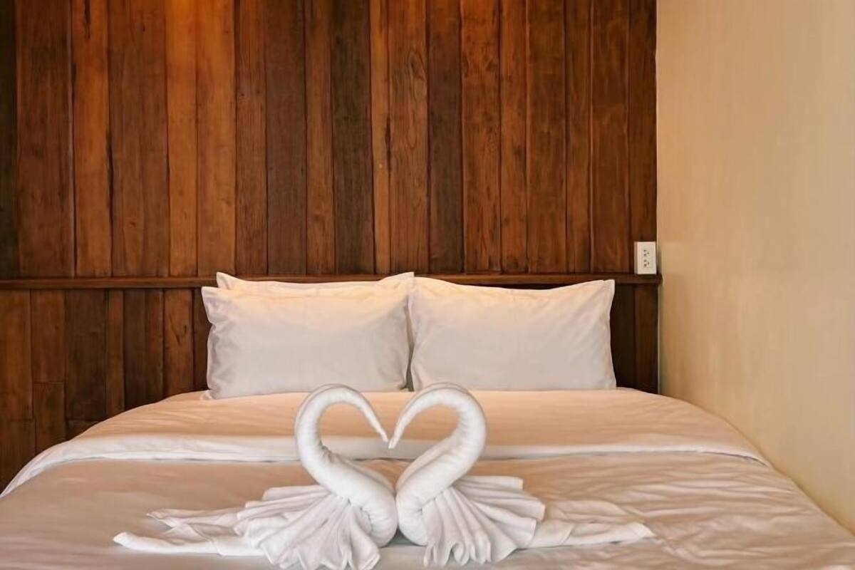 A bed with white linens and two swan-shaped towels arranged on it.