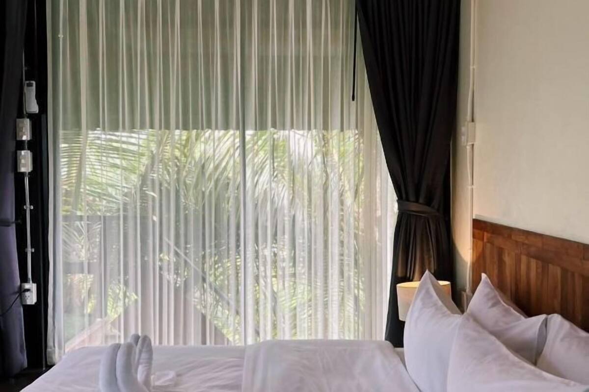 A bed with white linens, a wooden headboard, and sheer curtains.