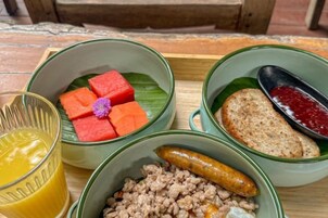A tray with bowls containing food items, a glass of juice, and a wooden bench in the background.