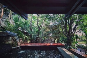 Un espace extérieur paisible, doté d’une terrasse en bois, d’un petit élément décoratif aquatique et d’une végétation luxuriante.