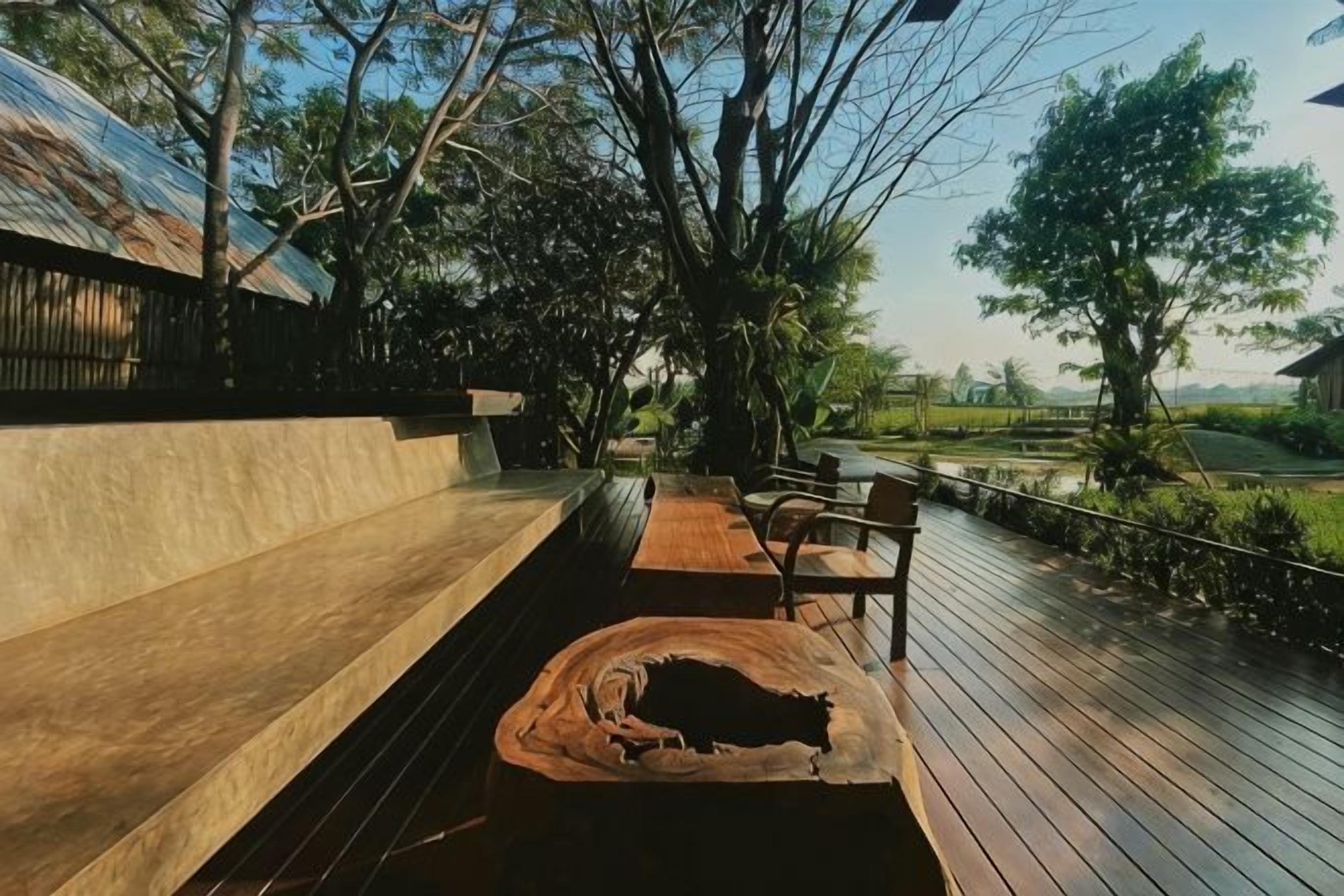 An outdoor deck with wooden benches and a rustic log seat, surrounded by trees and a view of a landscape.