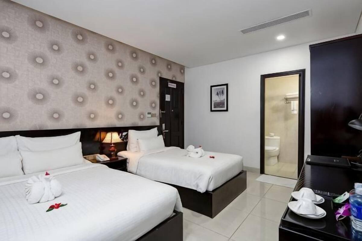 A hotel room with two beds, a large TV, a desk with a chair, and a bathroom visible through an open door.
