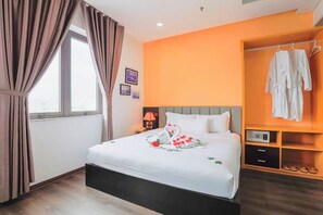 Una camera d'albergo con un letto, una finestra con tende, una parete arancione, un appendiabiti e un comodino.