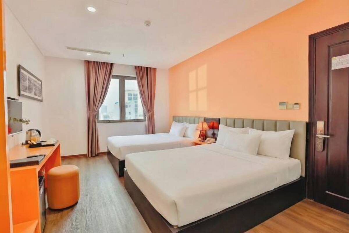 A hotel room with two beds, a desk, a chair, a window with curtains, and a door.