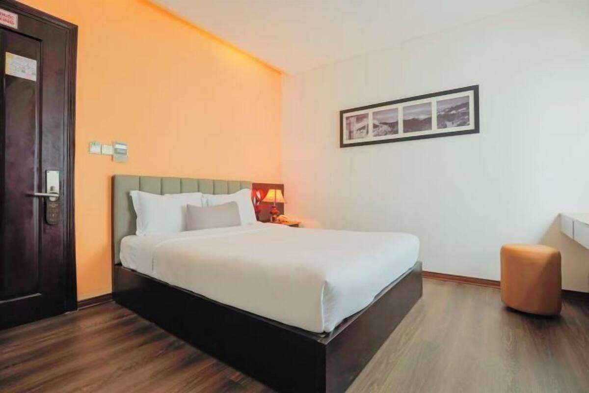 A hotel room with a bed, a nightstand, a desk, a chair, and a door.