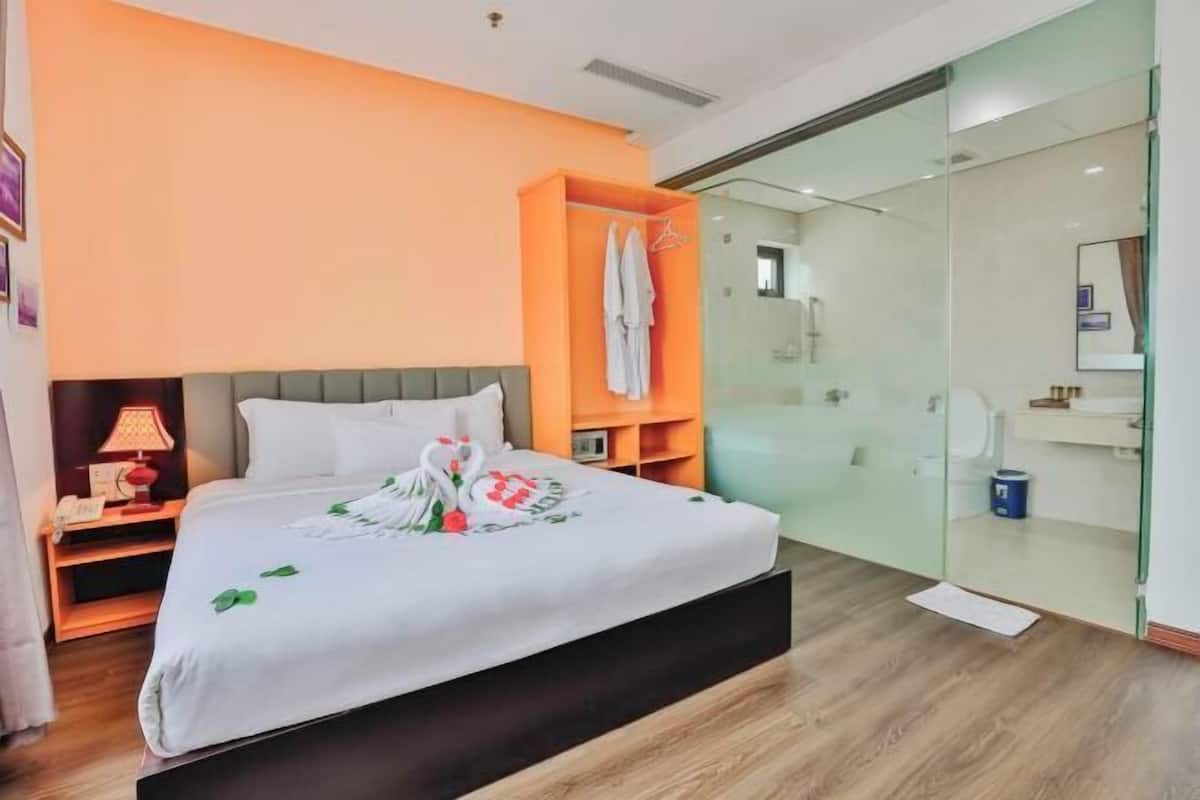 A hotel room with a bed, a nightstand, a glass-enclosed shower, and a small seating area.