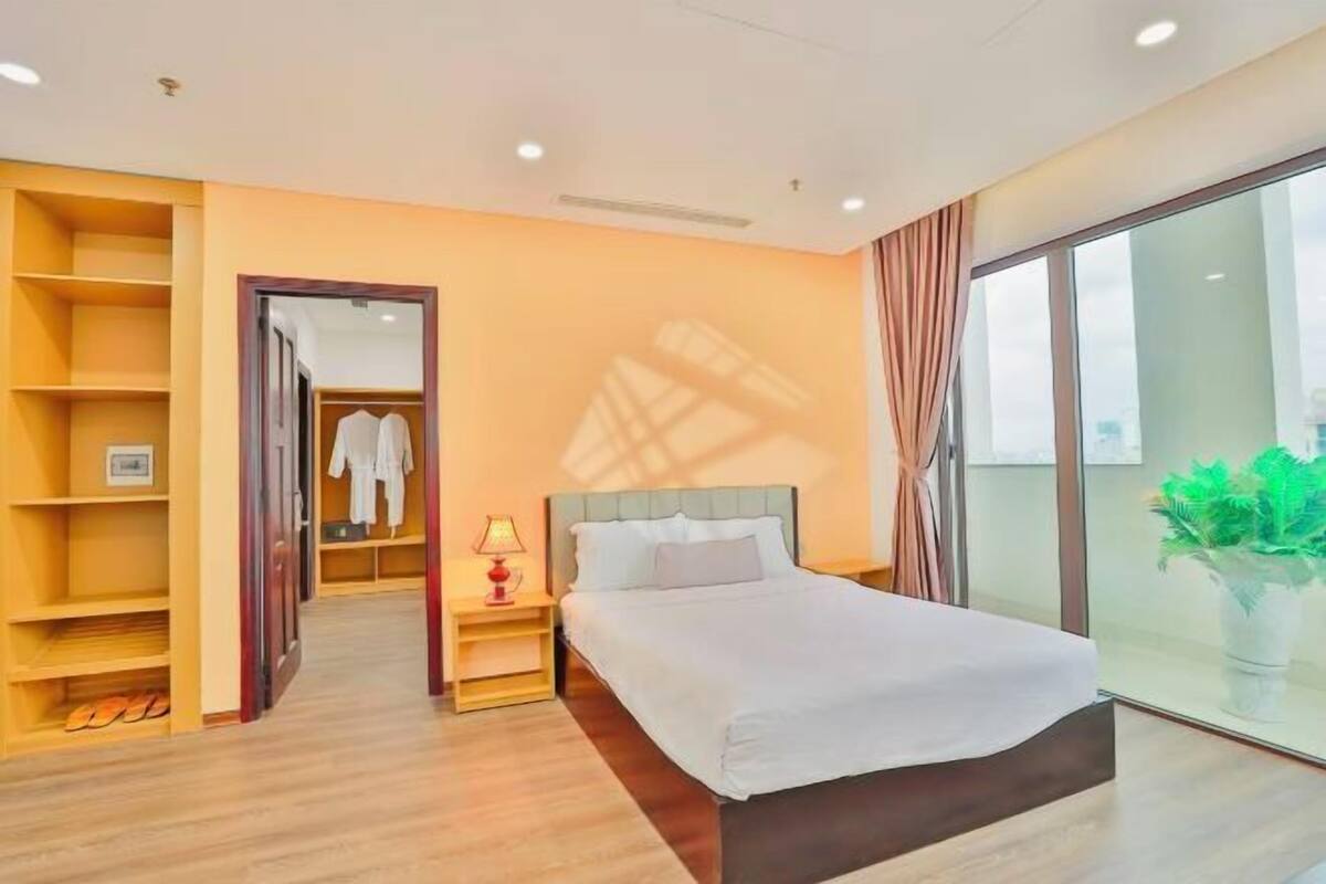 A hotel room with a bed, bedside table, lamp, wardrobe, and a large window.