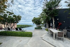 An outdoor terrace with tables and chairs, a river view, and a black wall with a red pipe. - Designer Suites George Town + LG Water Purifier【City View】 (Jelutong)