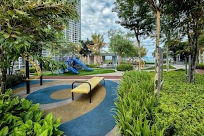 A playground with a slide and climbing structure, surrounded by greenery and a bench. - Designer Suites George Town + LG Water Purifier【City View】 (Jelutong)