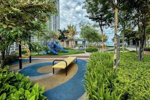 A playground with a slide and climbing structure, surrounded by greenery and a bench. - Designer Suites George Town + LG Water Purifier【City View】 (Jelutong)