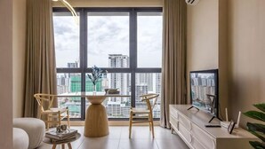 Ein modernes Wohnzimmer mit großem Fenster, einem Esstisch, Stühlen, einer Couch, einem Fernseher und einem Schrank.