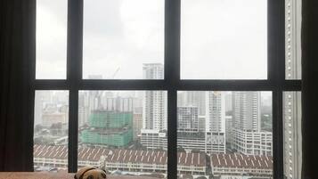 A bed with a plush toy, a window with a view of buildings, and curtains.
