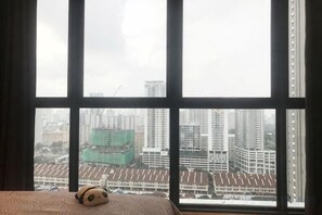 A bed with a plush toy, a window with a view of buildings, and curtains. - Designer Suites George Town + LG Water Purifier【City View】 (Jelutong)