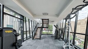 Ein Fitnessraum mit Trainingsgeräten, einer Treppe und großen Fenstern mit Blick auf die Stadt.