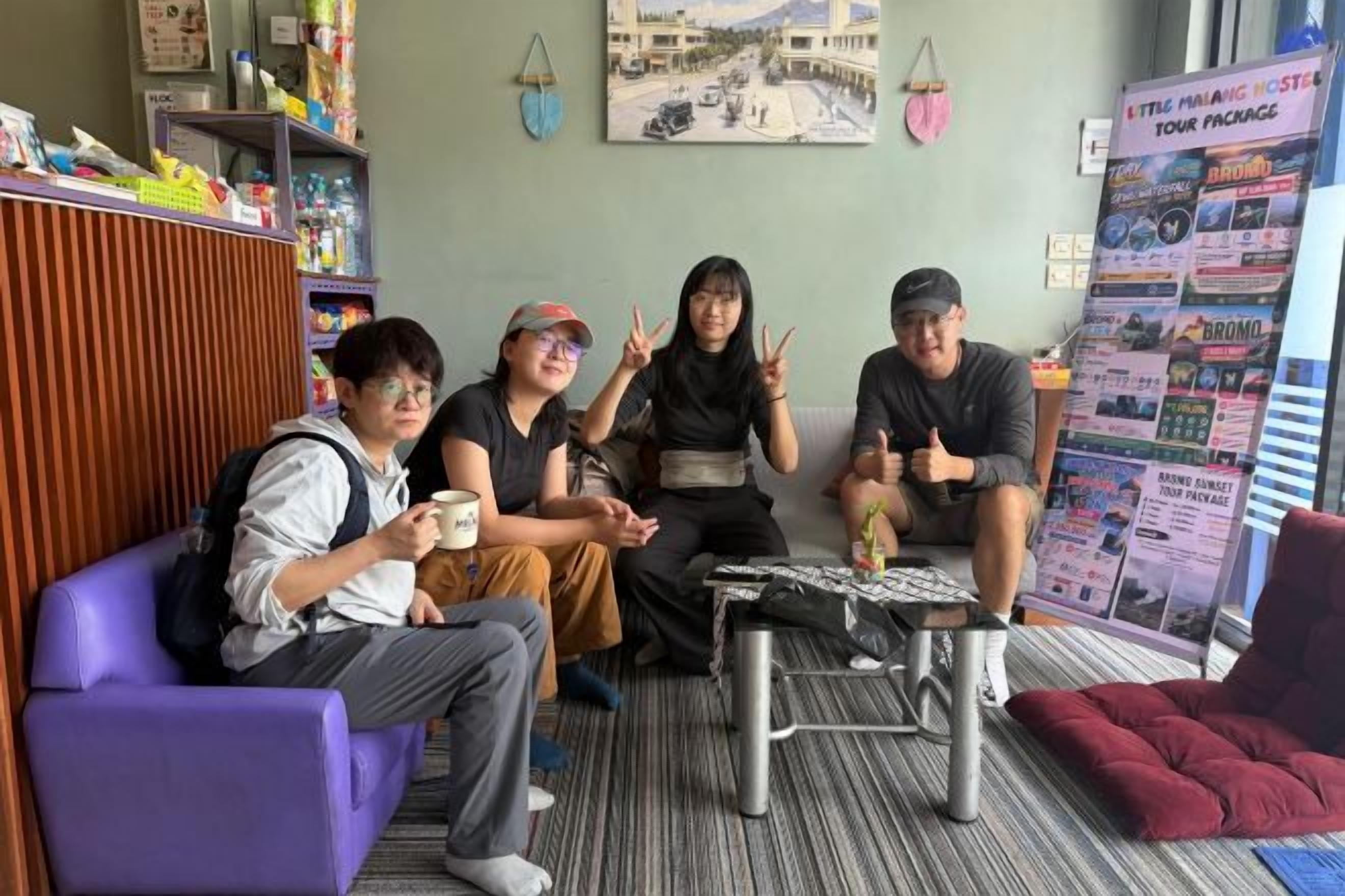 A group of people sitting on a couch and chairs in a room with a bulletin board and a small table.
