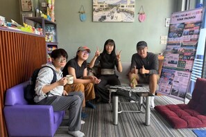 A group of people sitting on a couch and chairs in a room with a bulletin board and a small table. - Little Malang Hostel (Klojen)