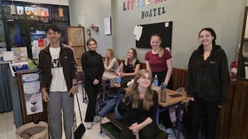 A group of people in a hostel room with a bed, a desk, and a wall with a sign.