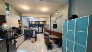 A hotel lobby with a reception desk, seating area, lockers, and a view of the restaurant. - Little Malang Hostel (Klojen)