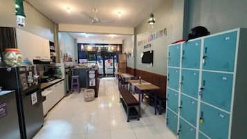 A hotel lobby with a reception desk, seating area, lockers, and a view of the restaurant.