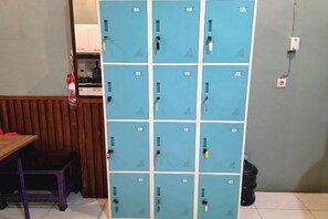 A row of blue lockers with a wooden bench and a trash bin in the foreground. - Little Malang Hostel (Klojen)