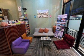 A reception area with a sofa, a small table, and a red armchair. There is a bulletin board with various notices. - Little Malang Hostel (Klojen)